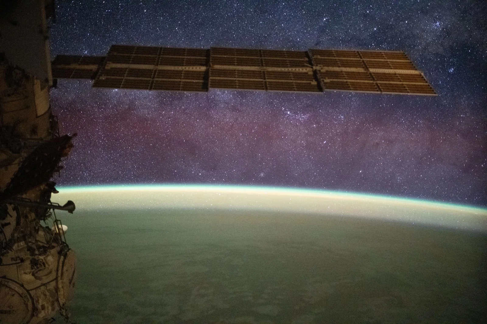 The Milky Way spans the night sky above a yellow-green airglow