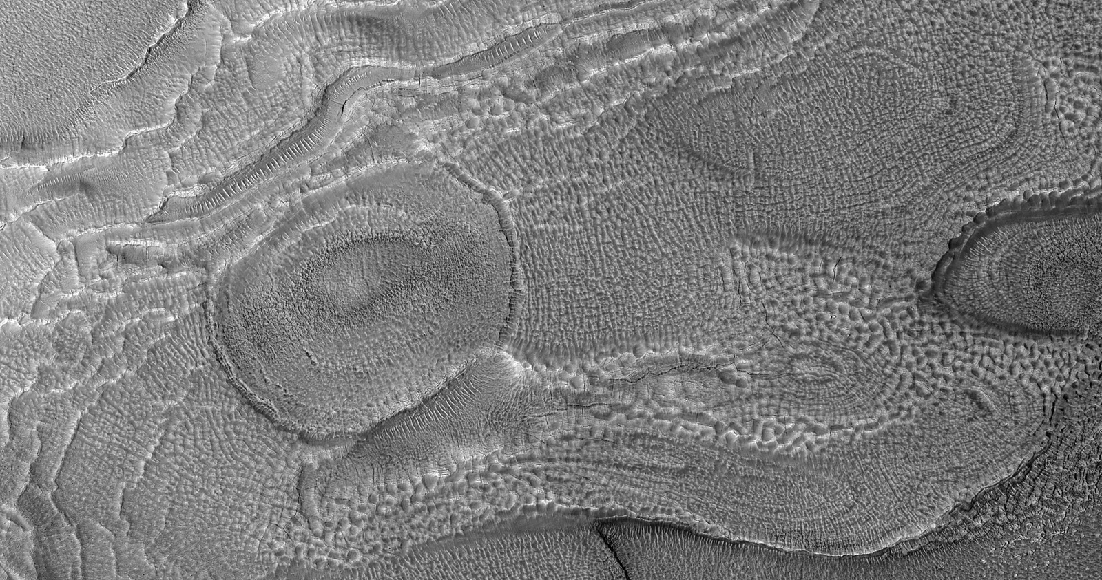 In a Context Camera image of this area, the crater floor has hollows and a high density of pits. The wall has the shape of the alcoves of gu