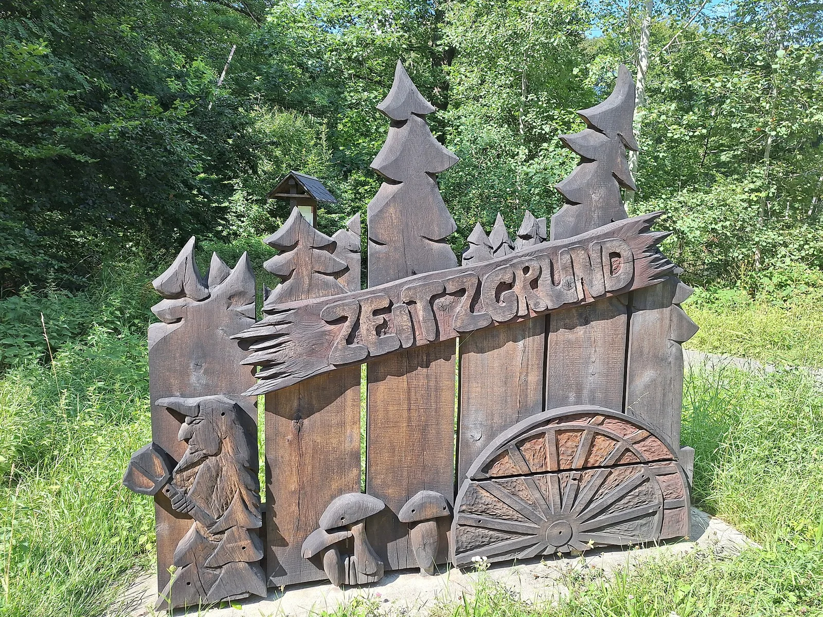 Carved wooden “Zeitzgrund” welcome sign on state road L 1076 near Mörsdorf, Thuringia, Germany. The wooden artwork depicts stylised conifer